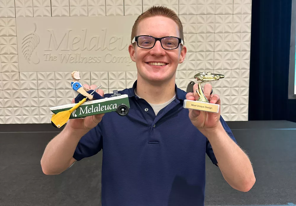 Man displaying the pinewood derby car and trophy he won